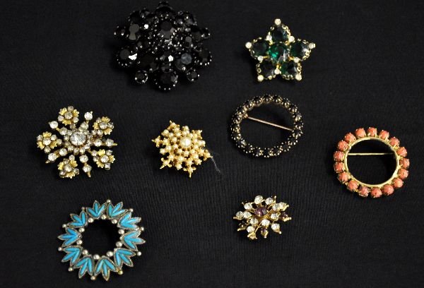 8Pc Costume Jewelry Broach Group: Includes a 2" onyx & metal broach, made in Austria; 4 rhinestone snow flake pins, one with amethyst stones & 3 pretty round pins. All show light signs of use & age. Examine photos or call for more inf