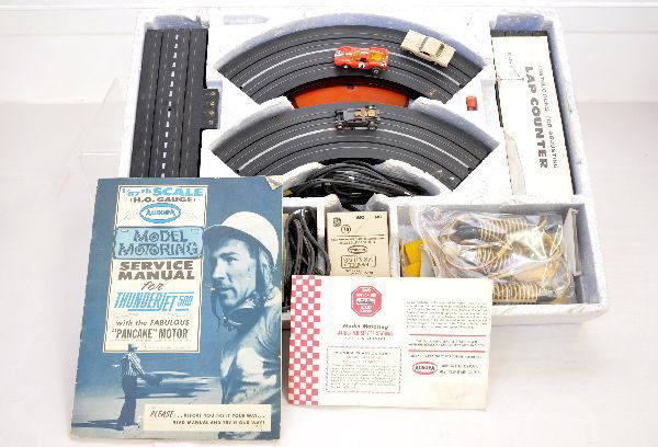 Boxed Aurora T-Jet Slot Car Set 1674: HO. Includes a Porsche, wheels cut and Cougar, missing its rear bumper with an extra chassis. The set includes a spiral climb & lap counter. It comes in a plain brown box with foam insert. It otherwis