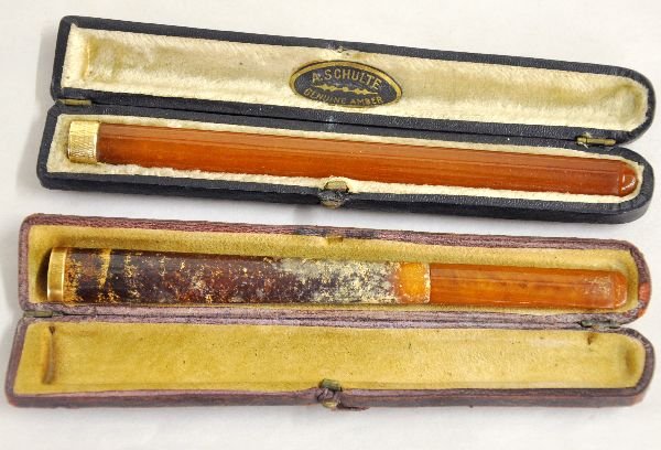Early Amber & 14K Gold Cigarette Holders: Unusual 6" long holders, both with stamped 14K gold ring tips. Solid example has a case marked A Schulte. The mottled version has been repaired, but are very unusual and have their original hard cases