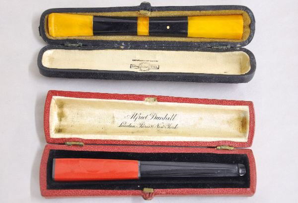 2 Unusual Dunhill Cigarette Holders: Includes a 4 1/2" amber & ebony holder with a 4 1/4" ebony & red Bakelite holder, red is cracking. Both show signs of use & age with hard cases. Examine photos, or call for more information