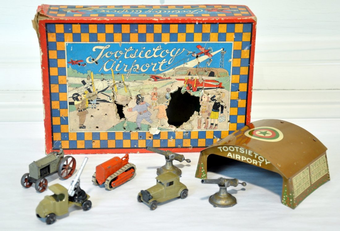 TootsieToy Military Lot: Includes C-cab Mack AA gun; tractor; Ford staff car; tractor, missing driver's head; tin airport hangar; 2 unmarked shore guns, partial setbox with insert, top rough. Toys show moderate playwear, C6-7