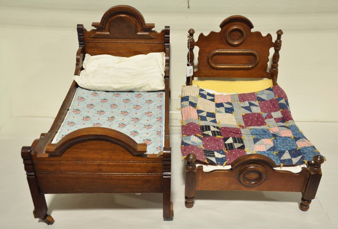 Two 19th Century Doll Beds: 26" oak sleigh bed style piece with original slats. It has original casters and includes a mattress & pillow and is in nice original condition. The 23" small bed is turned pine with walnut stain. It s
