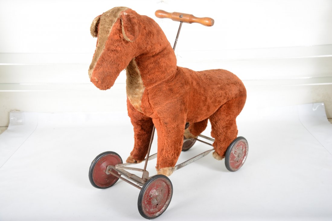 1920s Plush Ride-on Horse: 21" tall, excelsior filled wool horse on metal steerable structure with hard rubber tires. It has some damage around steering column and hoofs and its missing its eyes and tail. What is hear is remark