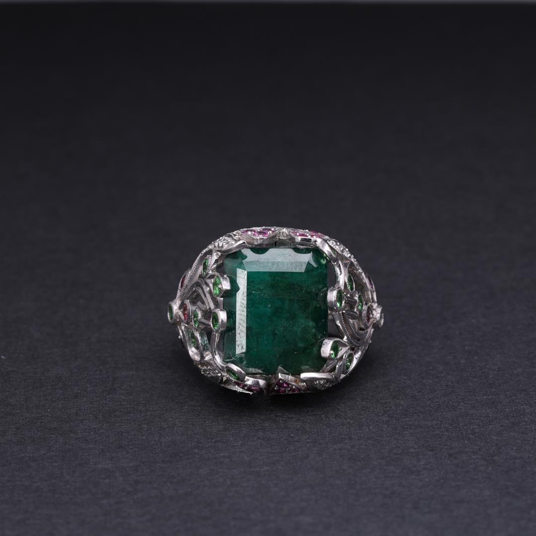 18k White Gold Emerald & Multistone Cocktail Ring by Victor Loo: Elaborate 18k white gold cocktail ring by Victor Loo; elaborate openwork designs of flowers and vines set with diamonds, emeralds and rubys surrounding a large center emerald, marked 18k to interior; 