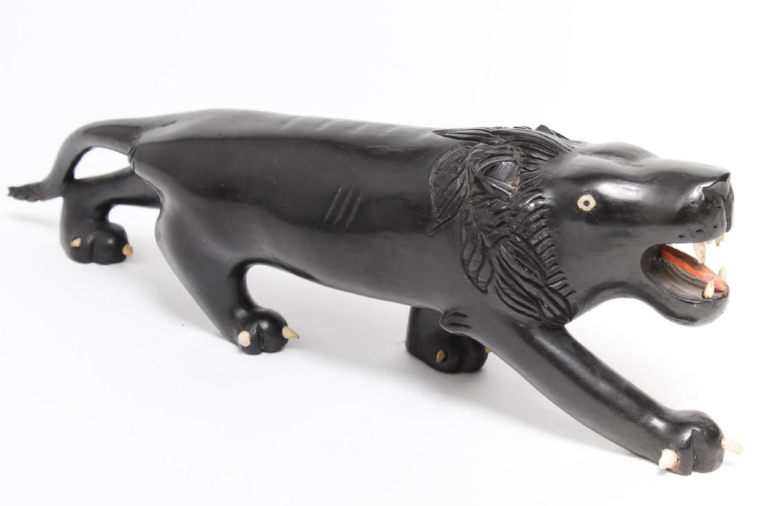 African Hand-Carved Ebony Prowling Lion: African ethnographic tribal art, carve wood lion with inset bone teeth, claws and eyes, and a red-stained tongue. 13.25" L. Lacking one claw on front paw, one broken on back paw.