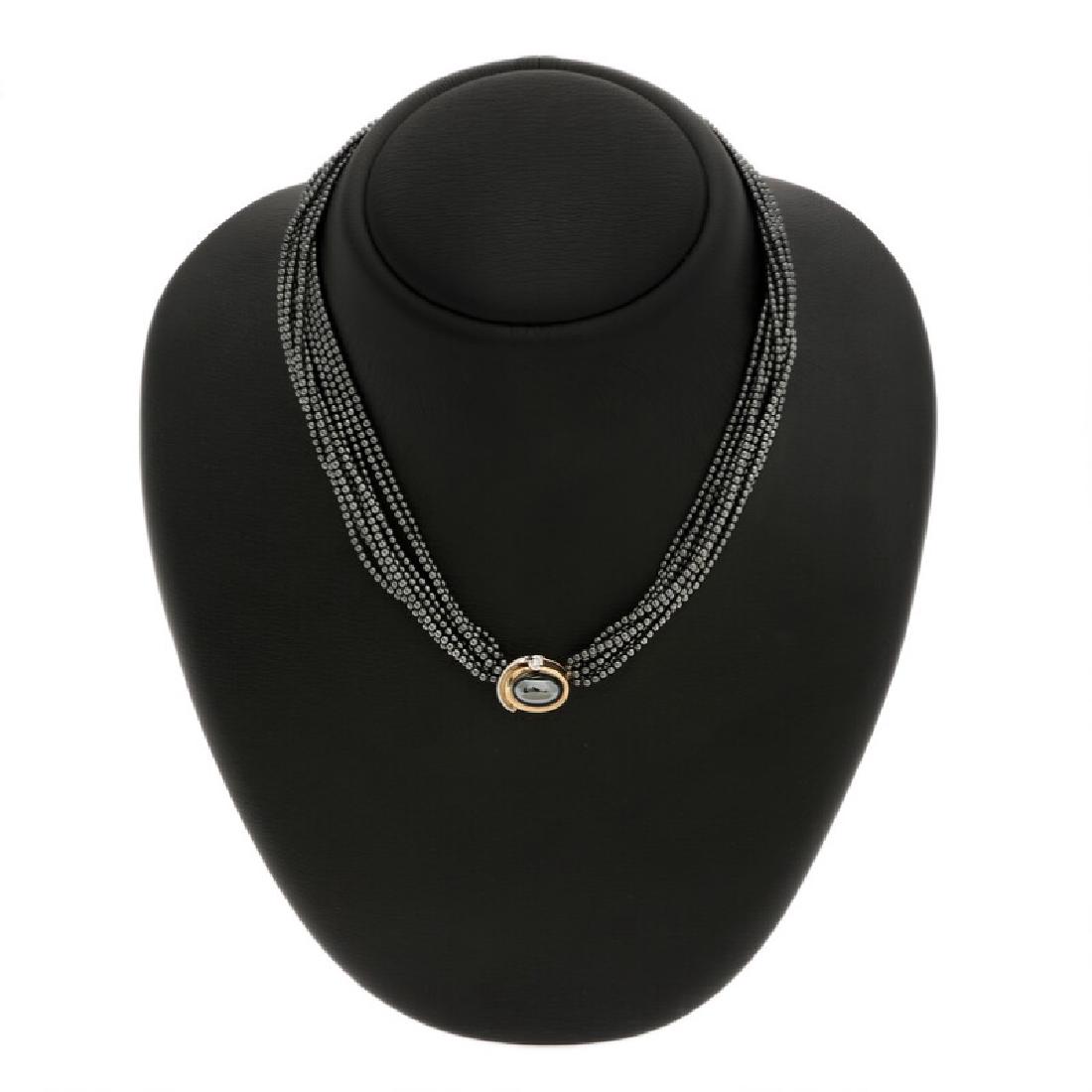 Ole Lynggaard: A hematite and diamond clasp set with a: A hematite and diamond clasp set with a cabochon hematite and a brilliant-cut diamond, mounted in 14k gold. Accompanied by two hematite necklaces. L. 47 and 41 cm. (3) Accompanied by box.