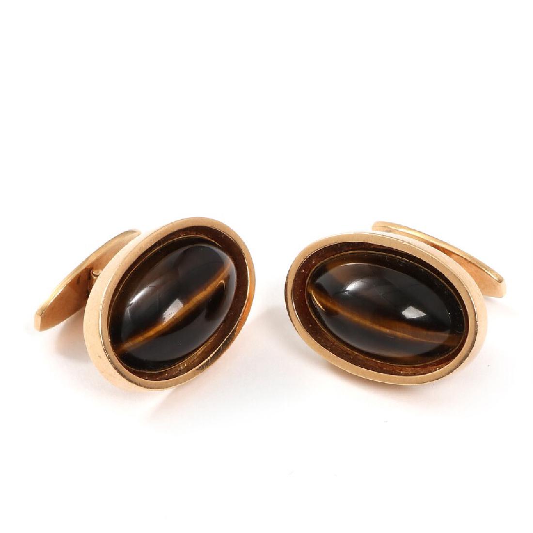 Bent Knudsen: A pair of tiger's eye cufflinks, set with: A pair of tiger's eye cufflinks, set with cabochon-cut tiger's eye, mounted in 14k gold. L. 2.4 cm. Weight app. 21.5 g. Circa 1970. (2) This lot is subject to Artist's Royalty. Artist’s Royalty In a