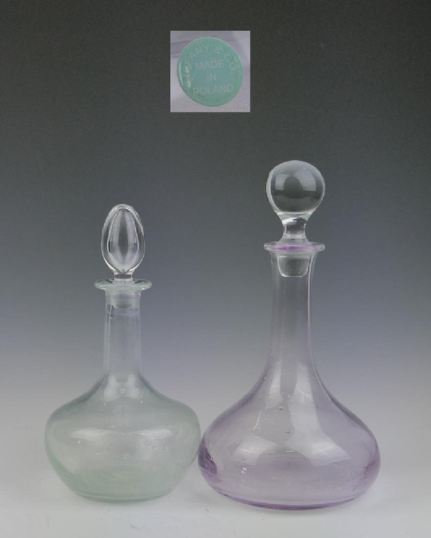 W YEOWARD & TIFFANY GLASS DECANTERS w STOPPERS: A lot of 2 vintage glass wine decanters with stoppers. One of a light cranberry glass by William Yeoward for Tiffany and Company (has acid mark and Tiffany label to bottom) and the next by Tiffany Com