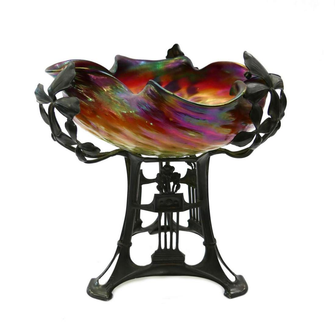 UNSIGNED LOETZ STYLE ART NOUVEAU CENTERPIECE BOWL: Unsigned Loetz style hand blown iridescent glass bowl having a ribbed exterior and ruffled rim. Bowl sets in an Art Nouveau bronze finish copper tripod floral stand. Measures approx. 12 1/2" height x