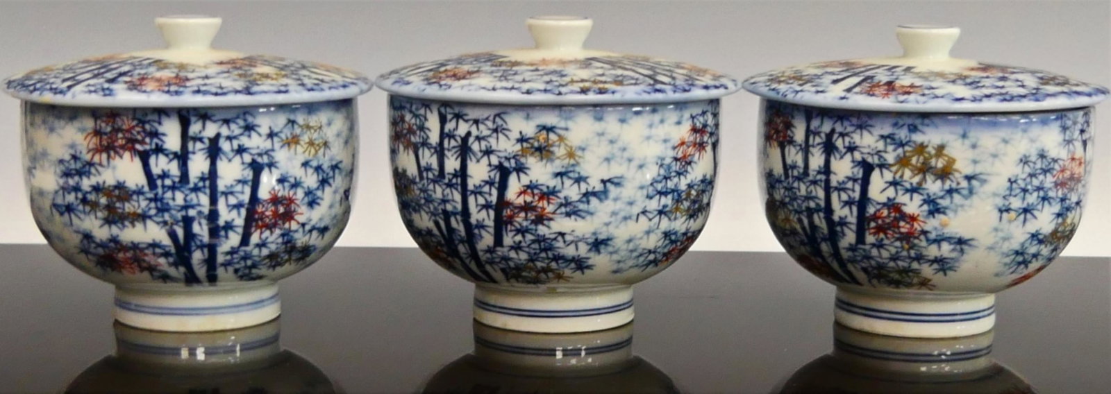 3 JAPANESE PORCELAIN BAMBOO COVERED TEA CUPS: A lot of three Japanese porcelain covered footed teacups having a bamboo design accented with hand painted gold and rust red leaves. Each with blue four character calligraphy stamp marks to bottoms. E