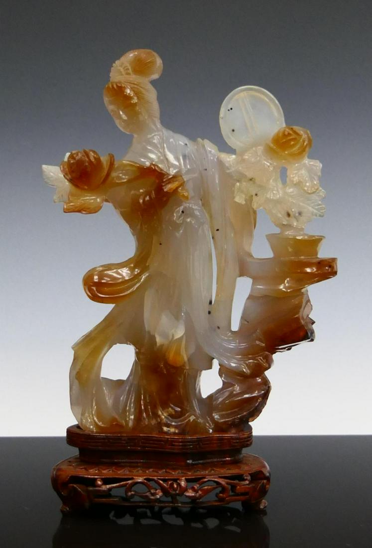 CHINESE CARNELIAN AGATE QUAN YIN SCULPTURE: Chinese carved carnelian agate sculpture depicting Guan Yin with peony blooms and fan. Includes fitted wooden display base. Measures approx. 7 1/4" height (18.4cm) overall including base. Total stone 