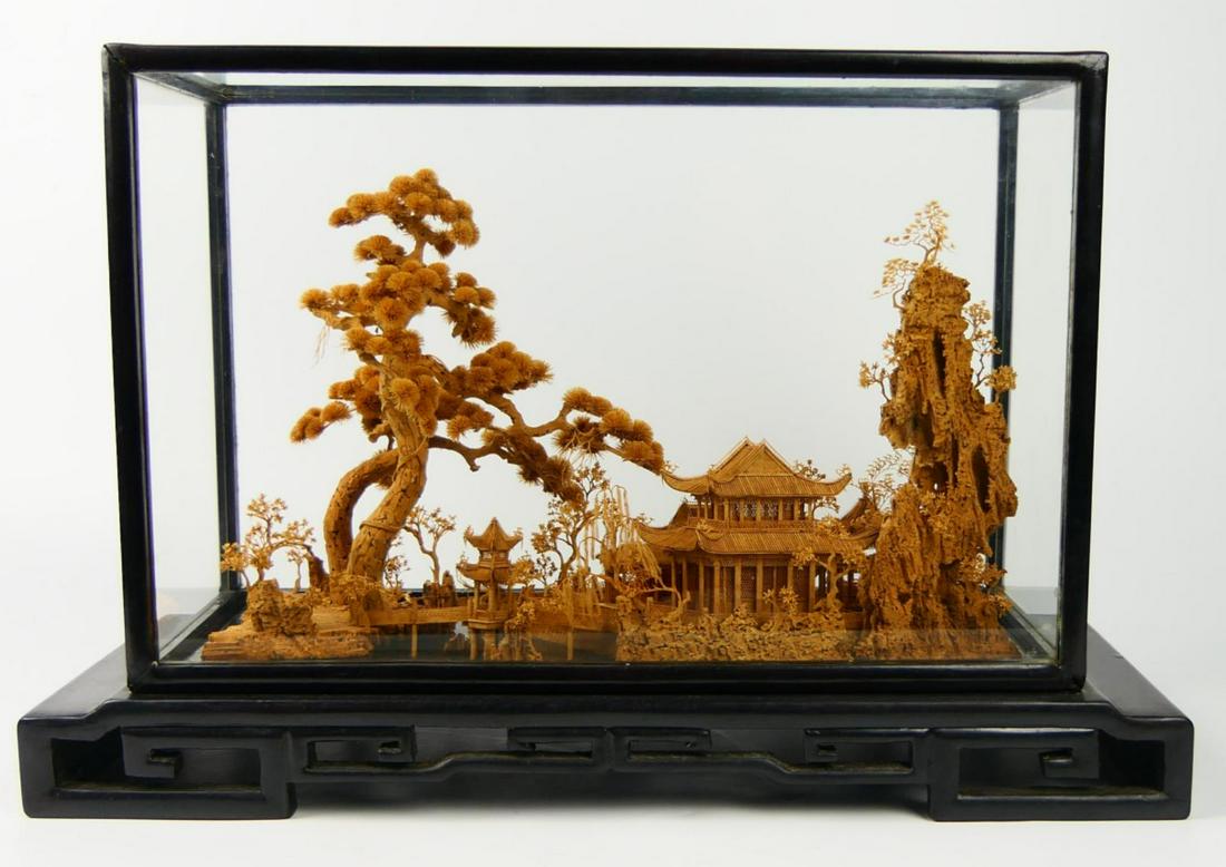 CHINESE BOXWOOD LANDSCAPE CARVING IN CASE: Chinese intricately carved box wood sculpture depicting a landscape scene with trees, pagodas and bridges. Rests on wooden base with key meander design and covered by glass and wood case. Measures app