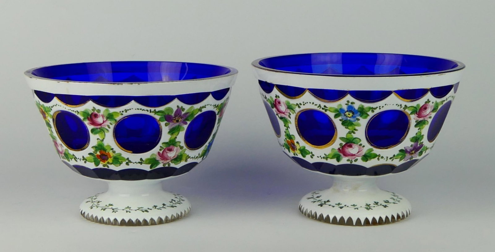 Pr ANTIQUE CONTINENTAL CUT TO COBALT GLASS BOWLS: A pair of antique Continental milk cut to cobalt glass footed bowls having hand painted enamel floral spray and leaf garland design. Each measures approx. 4 1/2" height x 6 1/4" diameter (11.4cm x 15.