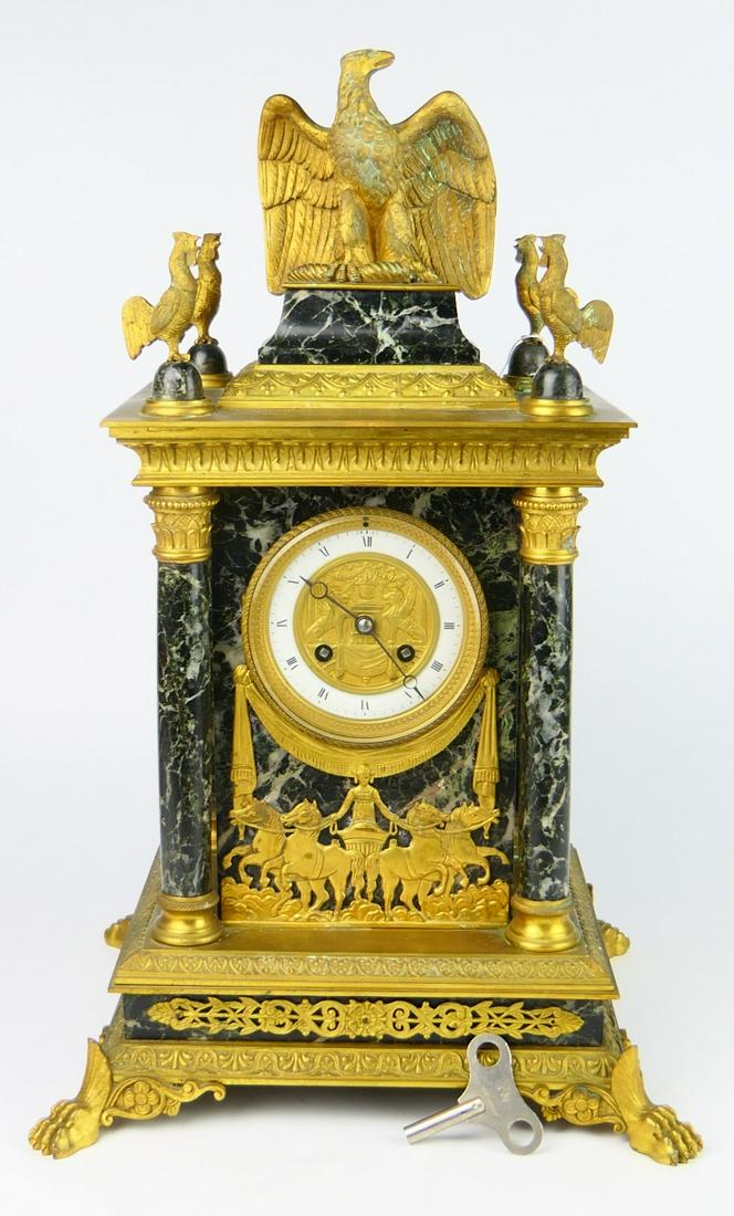 ANTIQUE SAMUEL MARTI FRENCH EMPIRE CLOCK: Bronze and marble Empire column shelf clock. Stands 19" tall to top of the eagle finial, has 4 lion feet. and 4 roosters to top. Bronze chariot scene to front of the clock white porcelain dial surroun