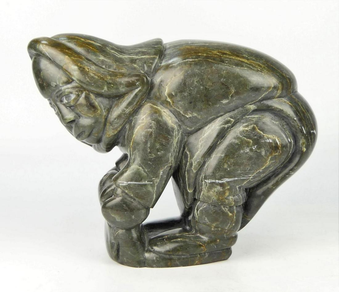 HEAVY DARK GREEN INUIT SCULPTURE OF MAN WITH OTTER: Heavy dark green stone Inuit carving depicting a man lifting an otter head. Signed to bottom and retains studio label. Measures approx. 10" height x 12 1/2" width (25.4cm x 31.7cm).