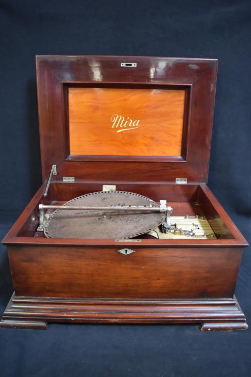 MIRA MUSIC BOX WITH 10 RECORDS: WORKING MIRA MUSIC BOX IN MAHOGANY CASE WITH 10 15 1/2 DISCS. SINGLE COMB PLAYER (HAS 4 BROKEN TEETH). 27 X 20 X 13