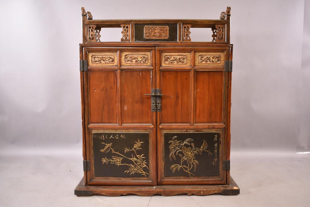 ANTIQUE 2 DOOR CHINESE ALTAR CABINET: HIGHLY CARVED -- BAT FIGURES ON TOP OF CABINET -- INTERIOR SHELVING -- METAL STRAPPING THROUGHOUT -- FLORAL DECORATION FRONT -- AGE WEAR AND SPLITS THROUGHOUT -- 39" x 29" x 45"