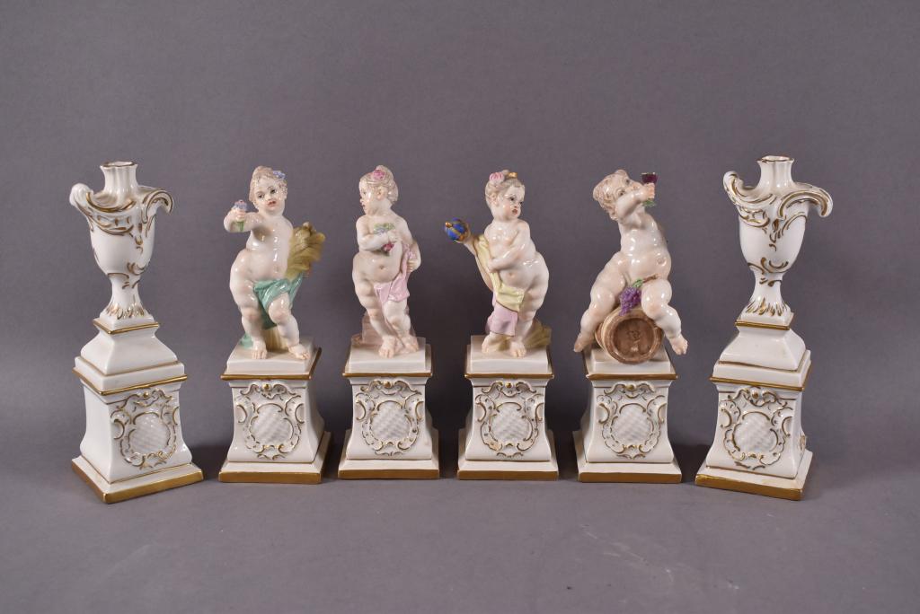 SET OF 6 MEISSEN STYLE FIGURES: 4 PUTTI FIGURES ON PEDESTALS & 2 URNS ON PEDESTALS. IMPRESSED SHIELD MARK AND NUMBERED ON BASE. PUTTI HOLDING WINE ON BARREL HAS DAMAGE TO BOTTLE TOP. 6 1/4" H