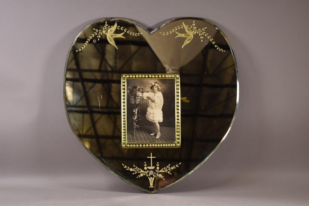1920'S ETCHED HEART SHAPE MIRROR WITH PHOTOGRAPH: MISSING 2 OF GLASS SCREW COVERS. HEART SHAPED. SMALL CHIPS TO BACK SIDE OF MIRROR EDGE. SILVERING LOSS. 24" x 23"