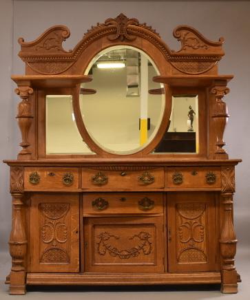 LARGE 1900'S AM. OAK SIDEBOARD: HIGHLY CARVED WITH LARGE OVAL BEVELED BACK MIRROR. 4 DRAWERS, 3 DOORS. 2 PART SIDEBAORD. MINOR WEAR TO FINISH, MISSING 6 OF SAWTOOTH CARVINGS ON TOP. WITH KEY. 66" W x 25 1/2" D x 85" H. THIS ITEM EXC