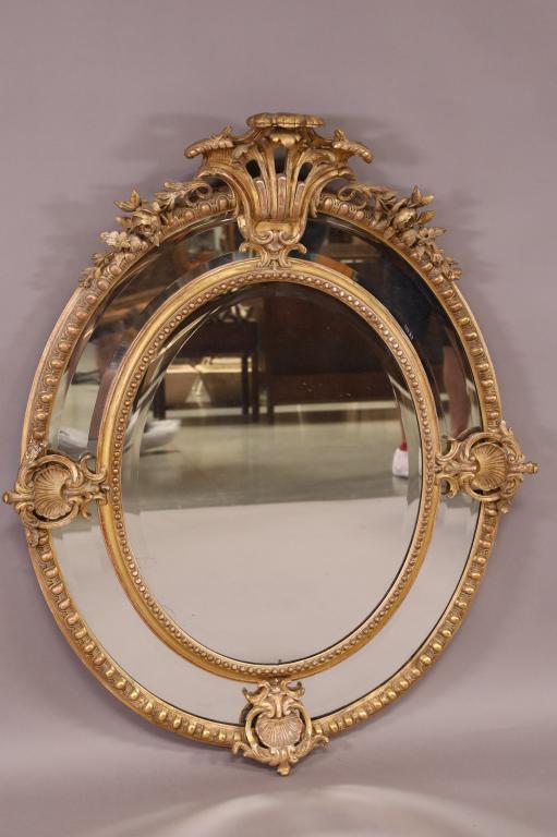 OVAL BEVELED WALL MIRROR: GILT WOOD AND GESSO BEVELED WALL MIRROR, ROSE AND SHELL DESIGN. MINOR DAMAGE TO FRAME. 37" W x 46" H. THIS ITEM EXCEEDS SIZE LIMITATIONS FOR IN HOUSE SHIPPING.