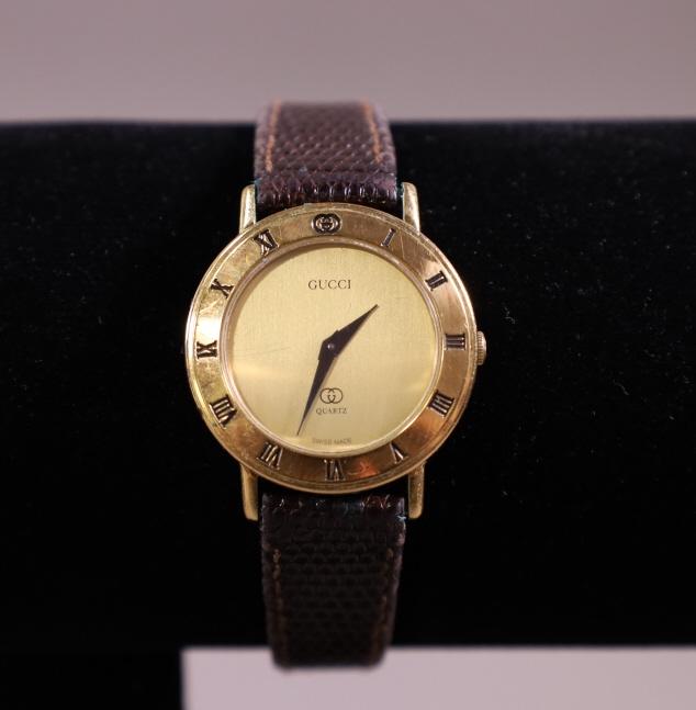 GUCCI LADY'S GOLD TONE WRISTWATCH: QUARTZ MOVEMENT WITH BROWN LEATHER STRAP, GUCCI LOGO ON BACK OF DIAL. 3001L. IN ORIGINAL BOX. ALL WATCHES ARE SOLD AS IS & ARE UNTESTED. WE DO NOT GUARANTEE WORKING ORDER.