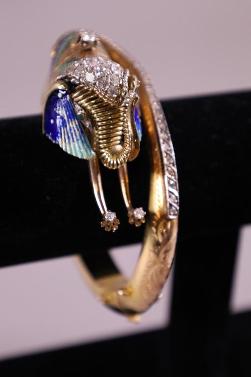 18 K GOLD AND ENAMELED ELEPHANT BRACELET: TESTED 18K GOLD & ENAMEL DECORATED ELEPHANT FORM BANGLE BRACELET. WITH 25 SMALL DIAMONDS ON SIDE. 12 DIAMONDS ON HEAD. 1/4 CARATS DIAMOND MOUNTED ON SADDLE. TWO DIAMONDS ON TUSK. APPROX 69 GRAMS.