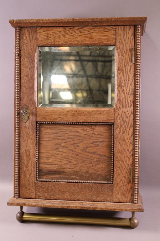 1910'S OAK HANGING MEDICINE CABINET: WITH TOWEL BAR. WITH KEY. GOOD CONDITION. 16 1/2" W x 22 1/2" H. THIS ITEM EXCEEDS SIZE LIMITATIONS FOR IN HOUSE SHIPPING.