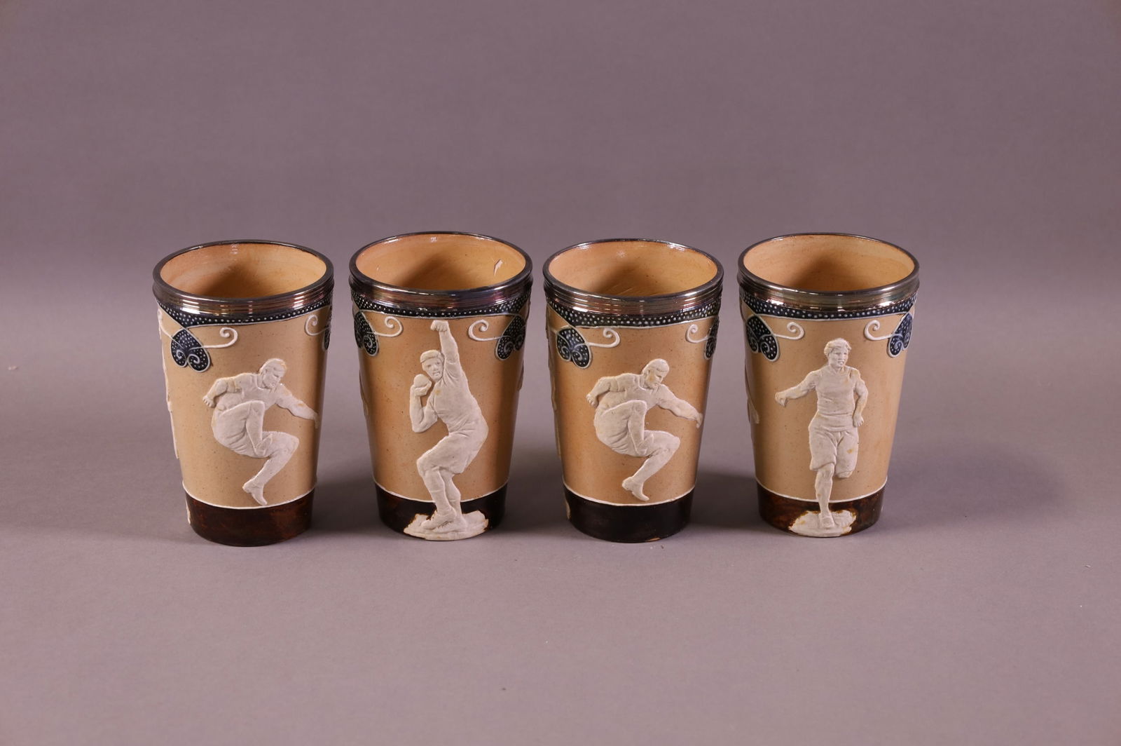SET OF FOUR DOULTON LAMBETH CUPS: STAMPED 9186. SILVERPLATE BANDED CUPS, THE OLYMPIANS. CRACK TO ONE. 5" H.