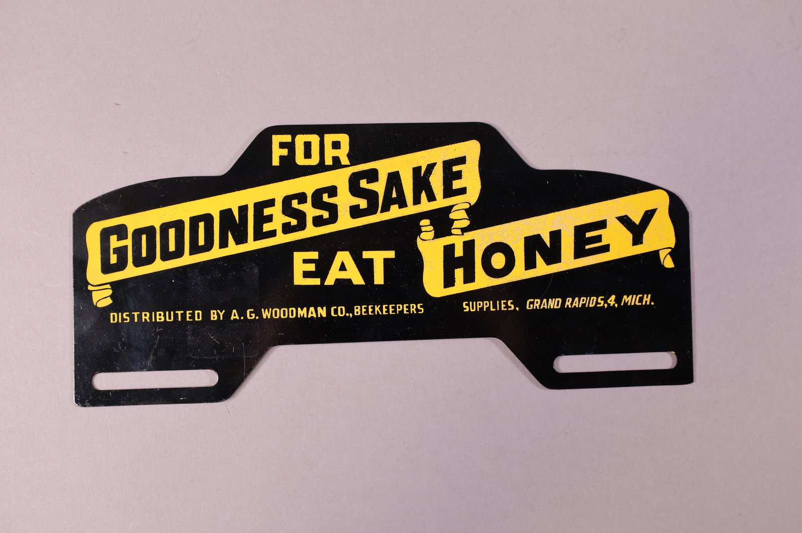 A.G. WOODMAN BEEKEEPERS TIN LICENSE PLATE TOPPER: FOR GOODNESS SAKE EAT HONEY A.G. WOODMAN CO BEEKEEPERS, GRAND RAPIDS MICH. GOOD CONDITION. 10" W x 4 1/4" H