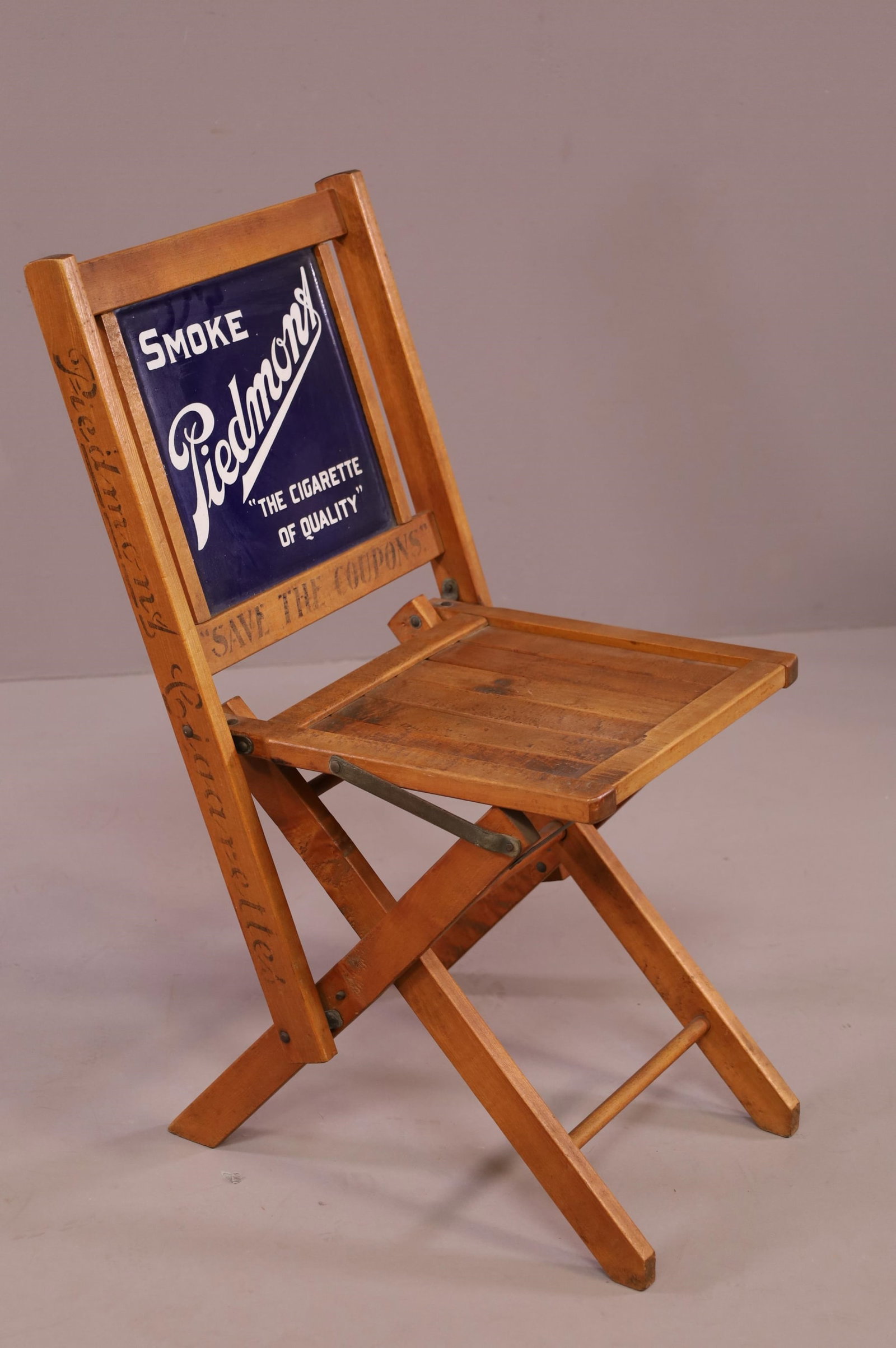 PIEDMONT CIGARETTES FOLDING CHAIR: WITH PORCELAIN SIGN INSERT, "SAVE THE COUPONS" 16" W x 20" D x 31" H. THIS ITEM EXCEEDS SIZE LIMITATIONS FOR IN HOUSE SHIPPING.