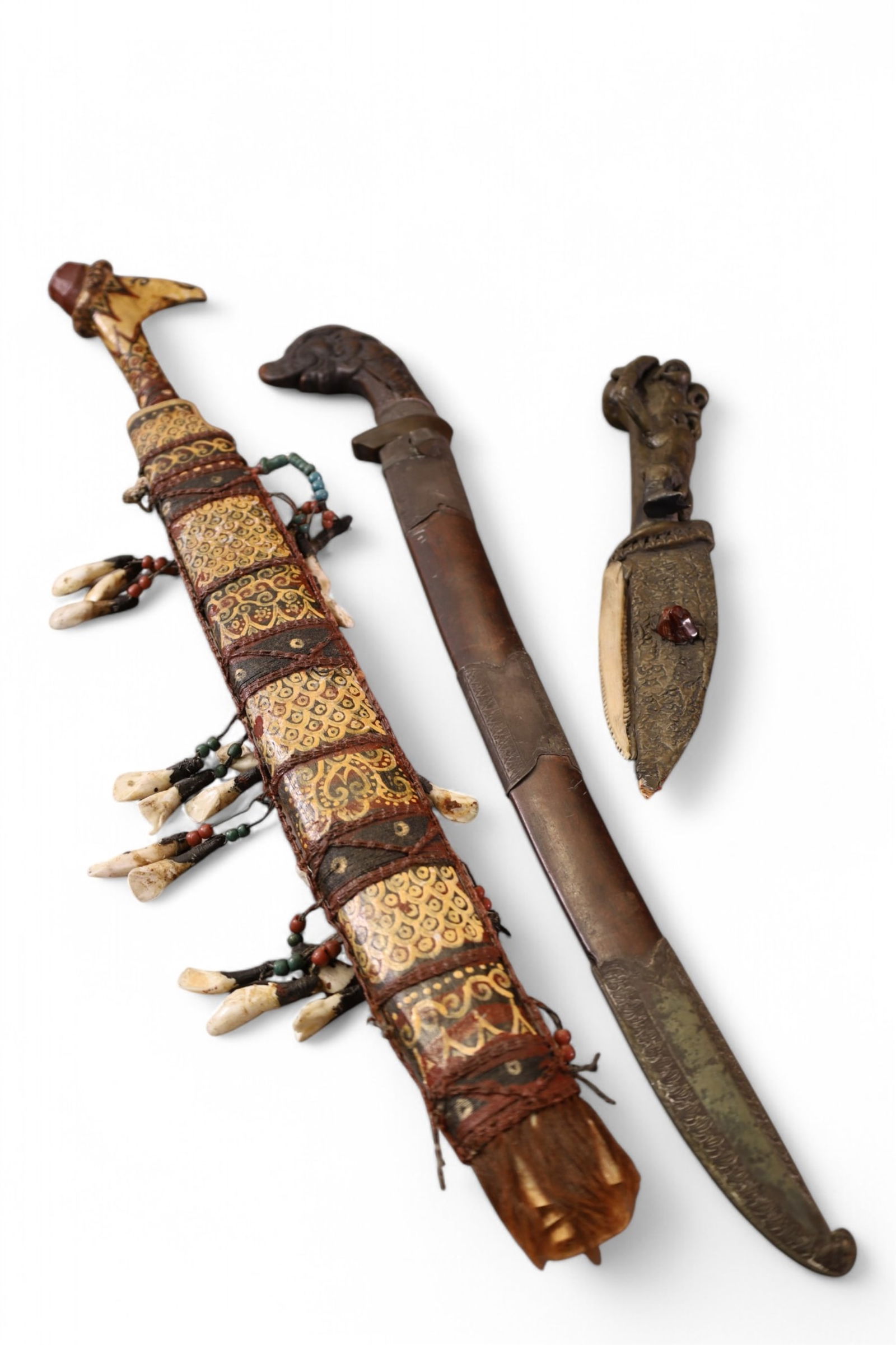 3 TRIBAL KNIVES: INDONESIAN PERANG, 24" L. TRIBAL BLADE IN SHEATH WITH TOOTH DECORATION, 24" L. & SMALL TRIBAL KNIFE. 11" L, MISSING ARM.