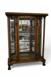 AMERICAN OAK CHINA CABINET: LARGE AMERICAN OAK BOWED GLASS CHINA CABINET WITH LEADED DOOR, LION CARVED DECORATION WITH LARGE PILLAR FRONTS. INTERIOR GLASS SHELVES. LARGE BALL AND CLAW FOOT. 54" W x 18" D x 72" H. THIS ITEM EXCEE
