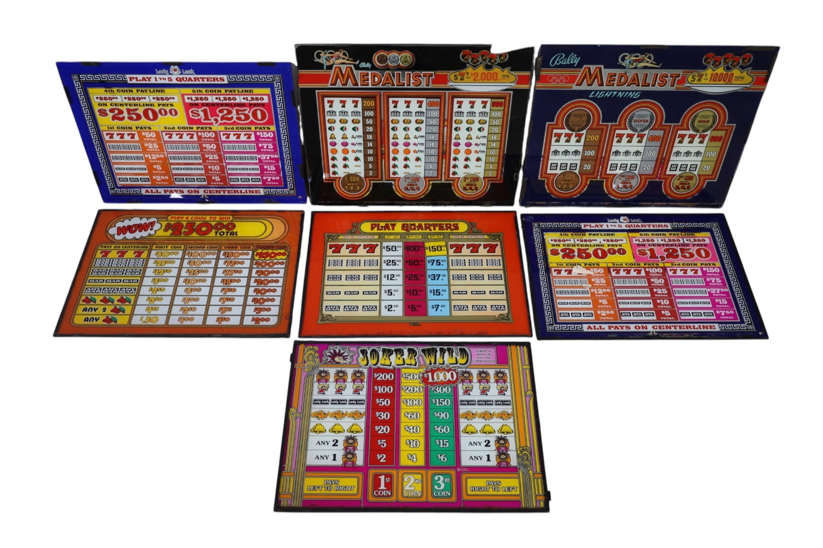 GROUPING OF SLOT MACHINE GLASS: VINTAGE SLOT MACHINE GLASS PANELS, INCLUDING, THE MEDALIST, JOKERS WILD, ALDY LUCK, AND MORE. 2 ARE BROKEN. APPROX 20" x 14"