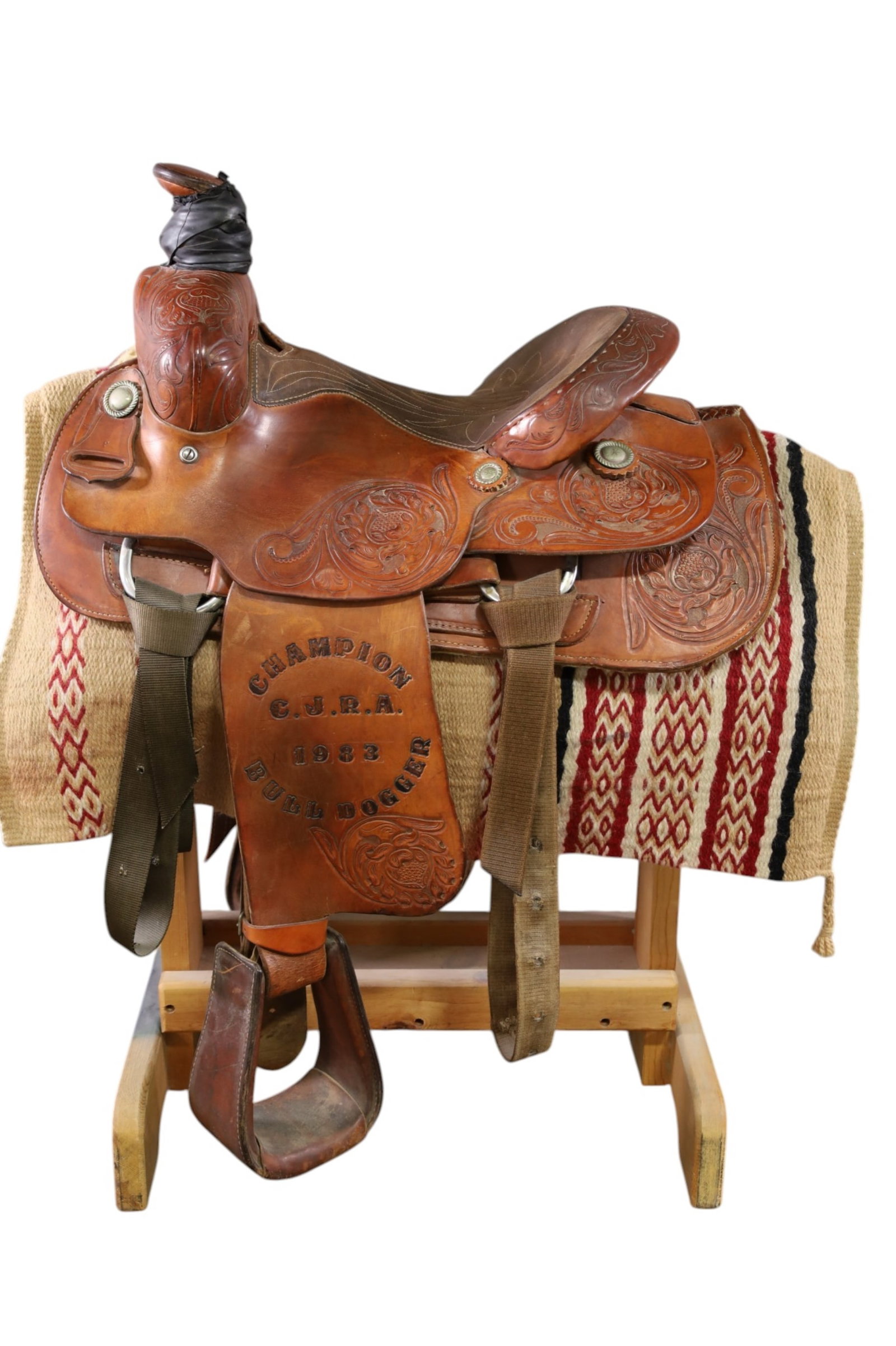 TOOLED LEATHER WESTERN SADDLE: MARKED C.J.R.A. 1983, CHAMPION BULLDOGGER. FROM COLORADO JR RODEO ASSOC. STEER WRESTLING SADDLE. 15" SADDLE. THIS ITEM EXCEEDS SIZE, WEIGHT, AND OR FRAGILITY LIMITATIONS FOR IN HOUSE SHIPPING, MUST
