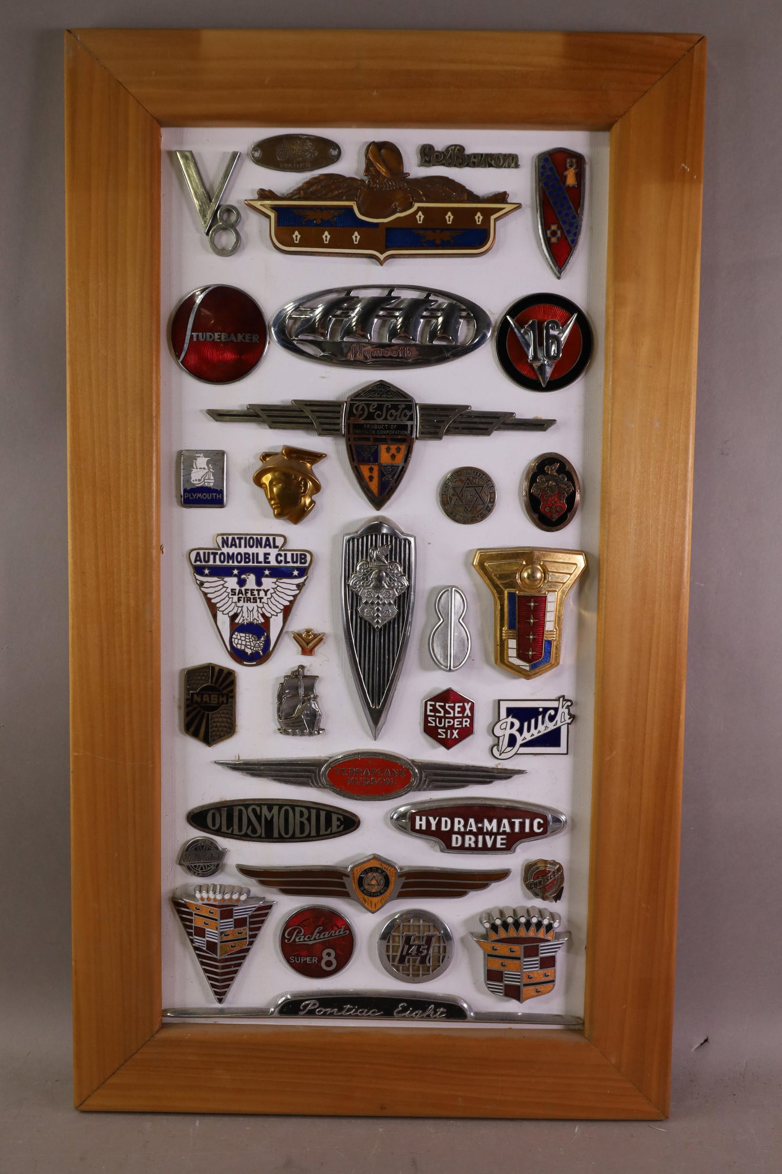 MISC CAR BADGES & EMBLEMS: 33 AUTOMOBILE BADGES AND EMBLES, GLUED OR BOLTED TO BOARD BACKING. 17 1/2" x 31"