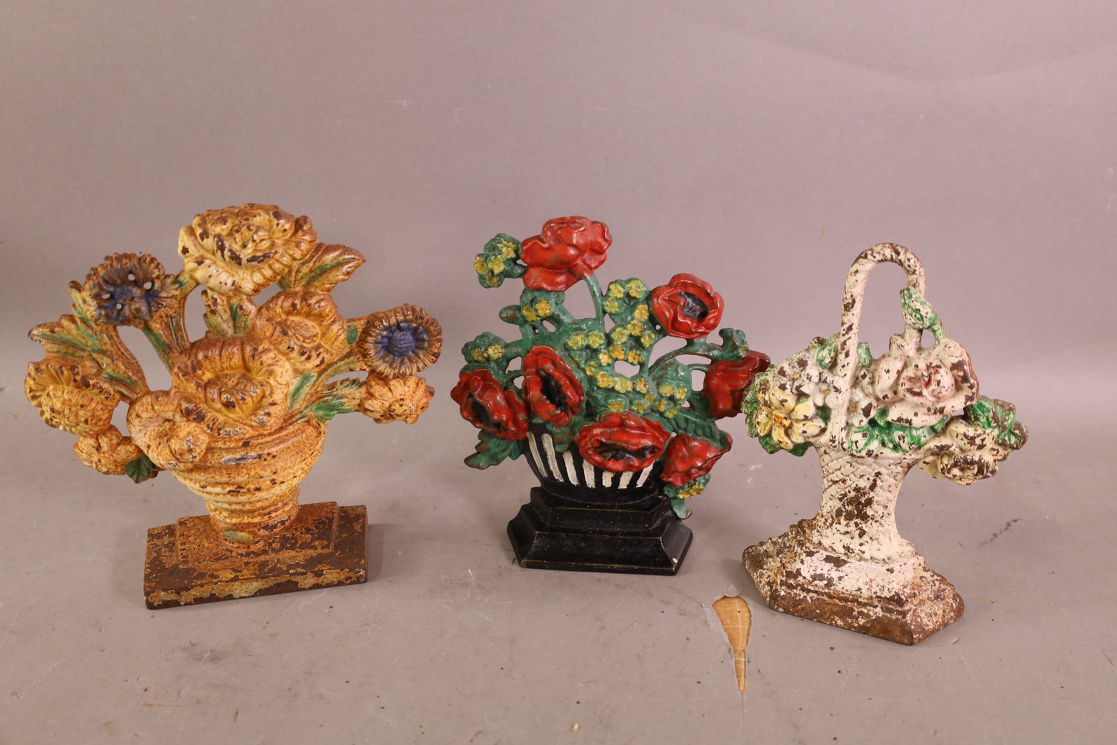 3 CAST IRON DOORSTOPS: FLOWER BASKET DOORSTOPS, ONE HAS BEEN REPAINTED. RUST & PAINT LOSS