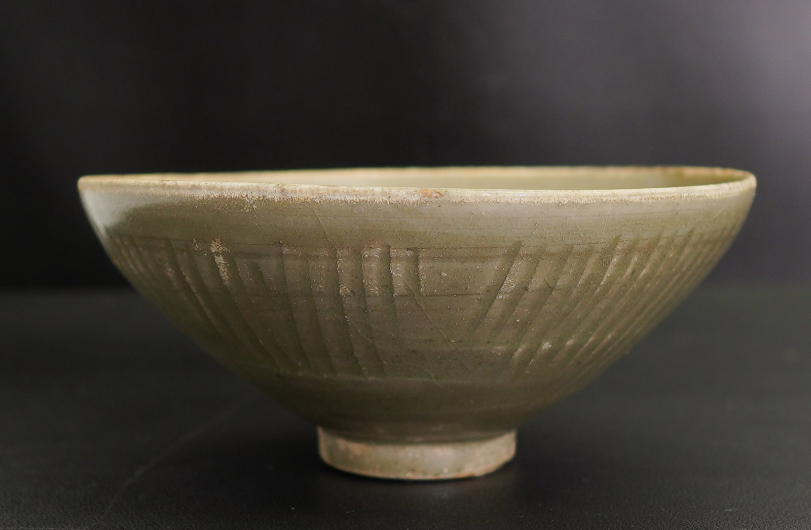 A CHINESE CELADON-GLAZED INCISED BOWL, NORTHERN SONG (960-1127): Size: 6" x 6" x 2 1/2". Description: Potted with gently curved sides rising from a short foot, the interior with incised and combed abstract motifs and covered in an olive-green glaze that pools to a 