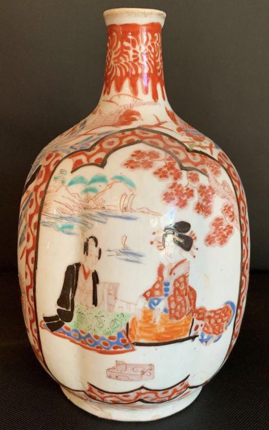 Rare Imari Sake Bottle, Late Edo Period: Six lobed sake bottle in traditional Imari palette with two cartouche featuring a samurai with a courtesan sharing a picnic lunch by a lake, the cartouche separated by a flock of cranes in pale blue.