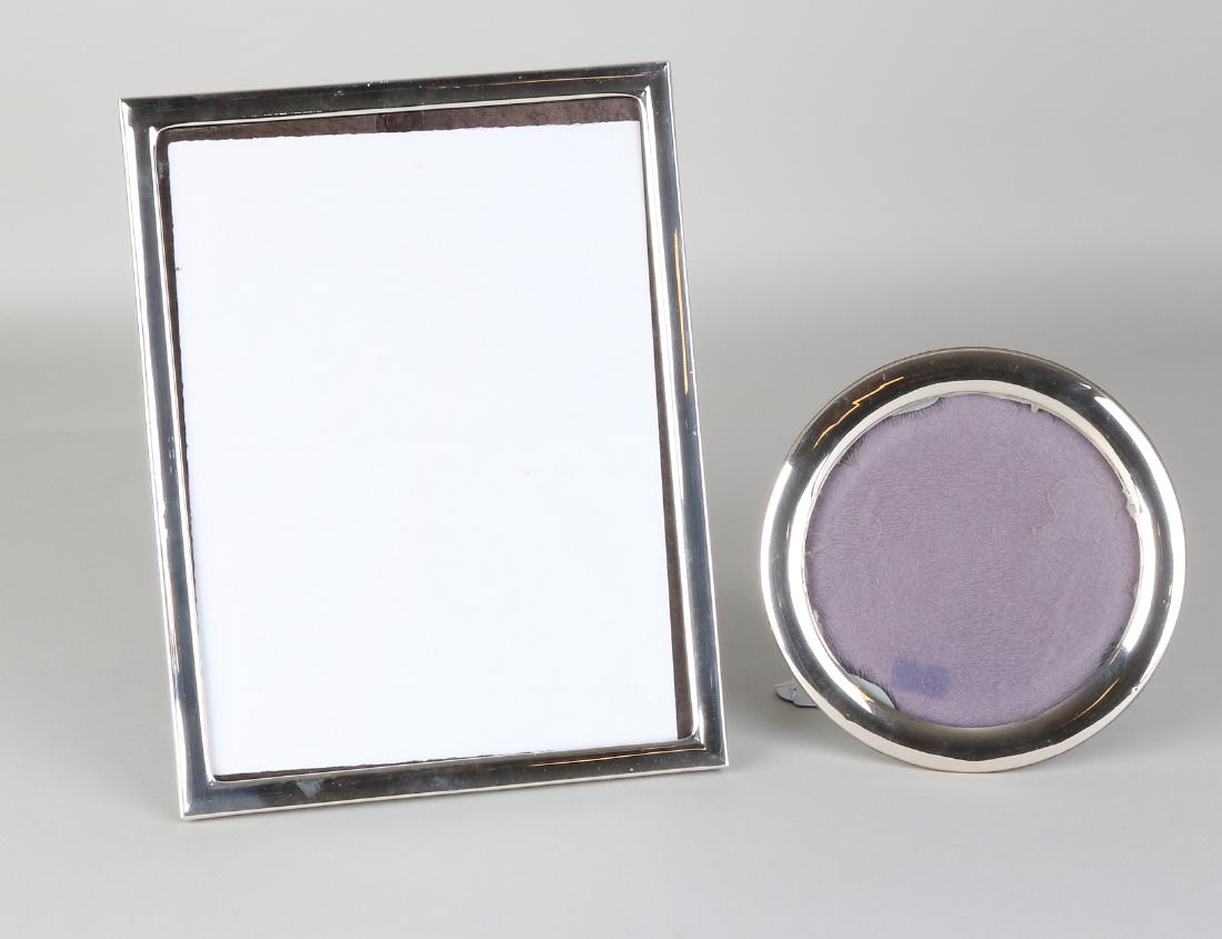 Two silver photo frames, 925/000, elongated frame with: Two silver photo frames, 925/000, elongated frame with silver cushions edge, 20x27cm and a round frame with round silver edge, ø16 cm. Round list is slightly dented, otherwise in good condition