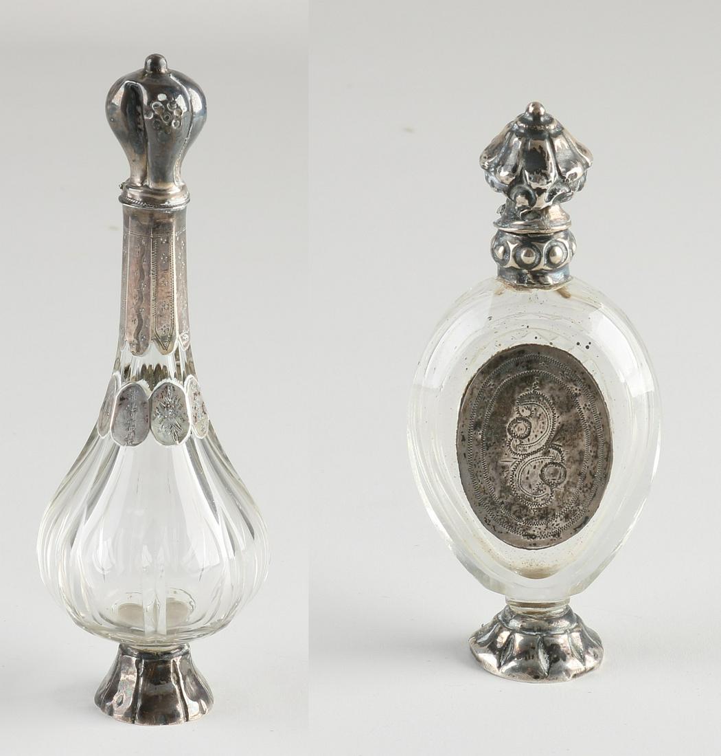 Two Odeur bottles: Two odeur flasks with silver, 833/000. Crystal odeur flacon, belly model, with grinding, placed on a 7-sided silver base with a long silver collar and convex cap with engraving. Also provided with a s