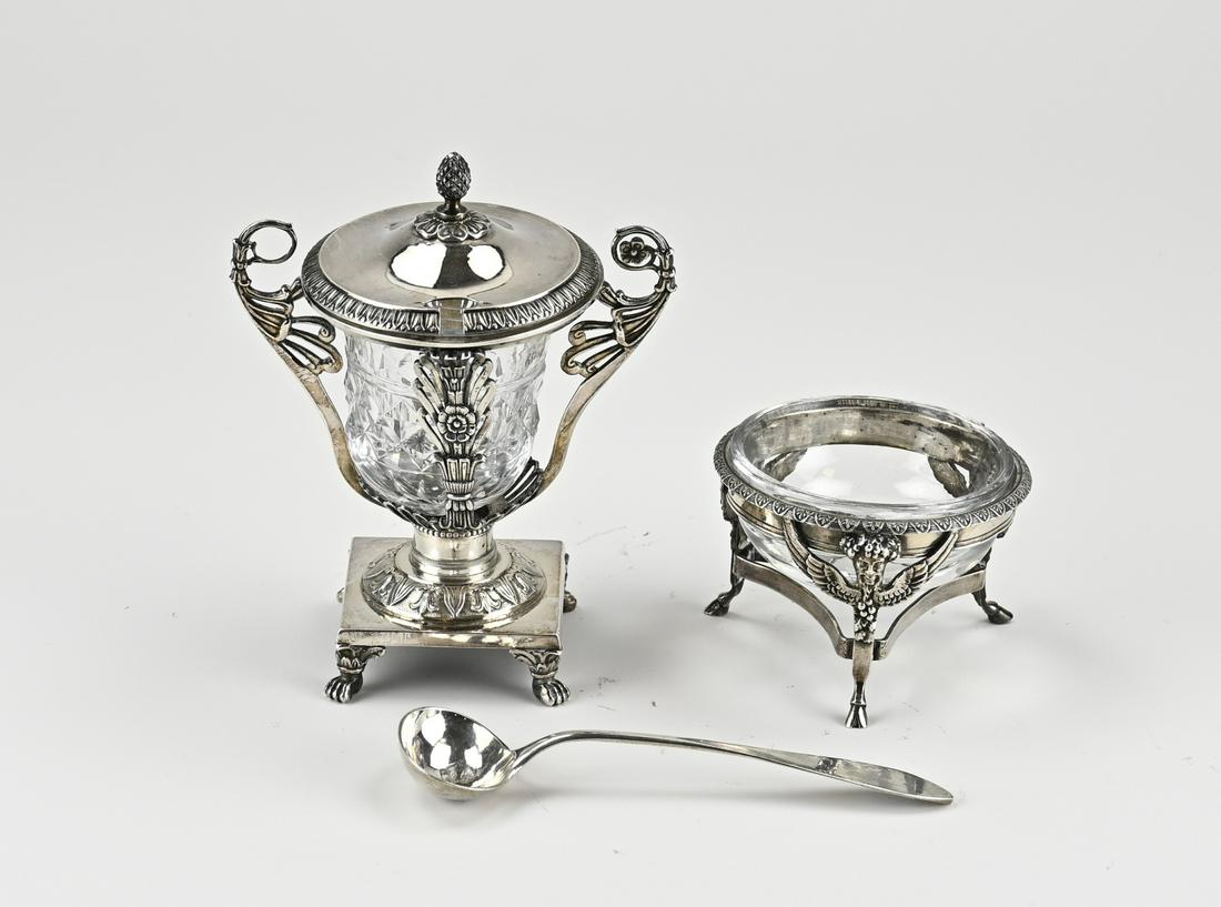 Mustard pot and salt shaker with silverware: Mustard pot and salt shaker with silverware. A crystal mustard pot with a silver frame decorated with floral decoration, placed on a round base with decorated rim and a square base with claw feet. The