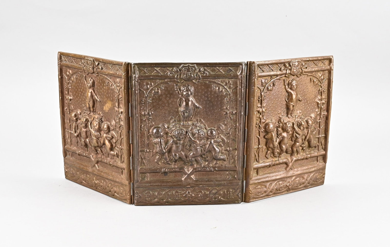 Small brass table screen, 1880: Antique historicism copper-beaten table screen, foldable. Putti decor. Circa 1880. Dimensions: H 22 x W 47 cm. In good condition.
