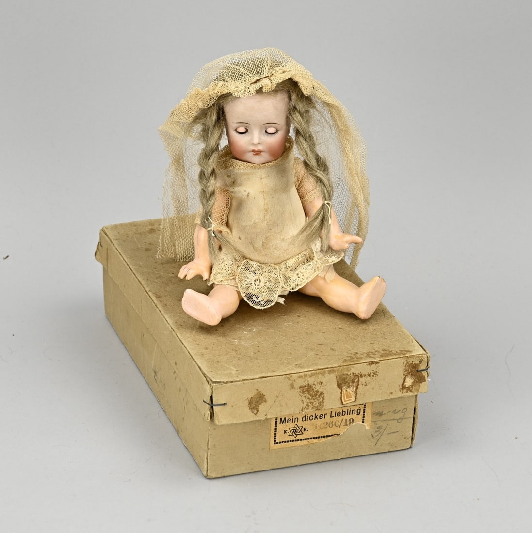 Antique doll in original box: Antique German porcelain doll in original box. Circa 1920. Kammer & Reinhard. 'Mein dicker Liebling'. No. 120. With mohair hair, baby body, sleep eyes and original clothing. Size: 21 x 12.5 x 6 cm.