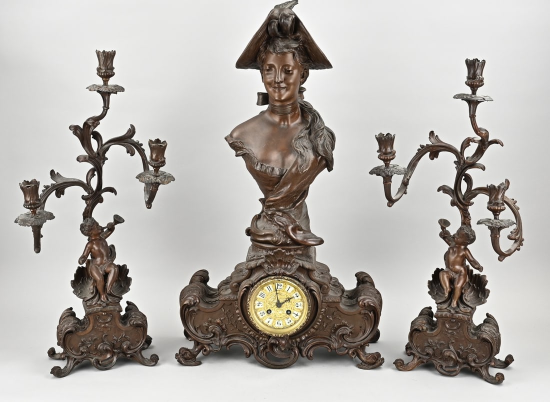 Antique Art Nouveau clock set, 1900: Antique Art Nouveau clock set with large bust of a lady and bachus. Composition metal. Bronze-coloured. Eight-day movement, half-hourly striking of St. Marti. Dimensions: 61 - 70 cm. In good