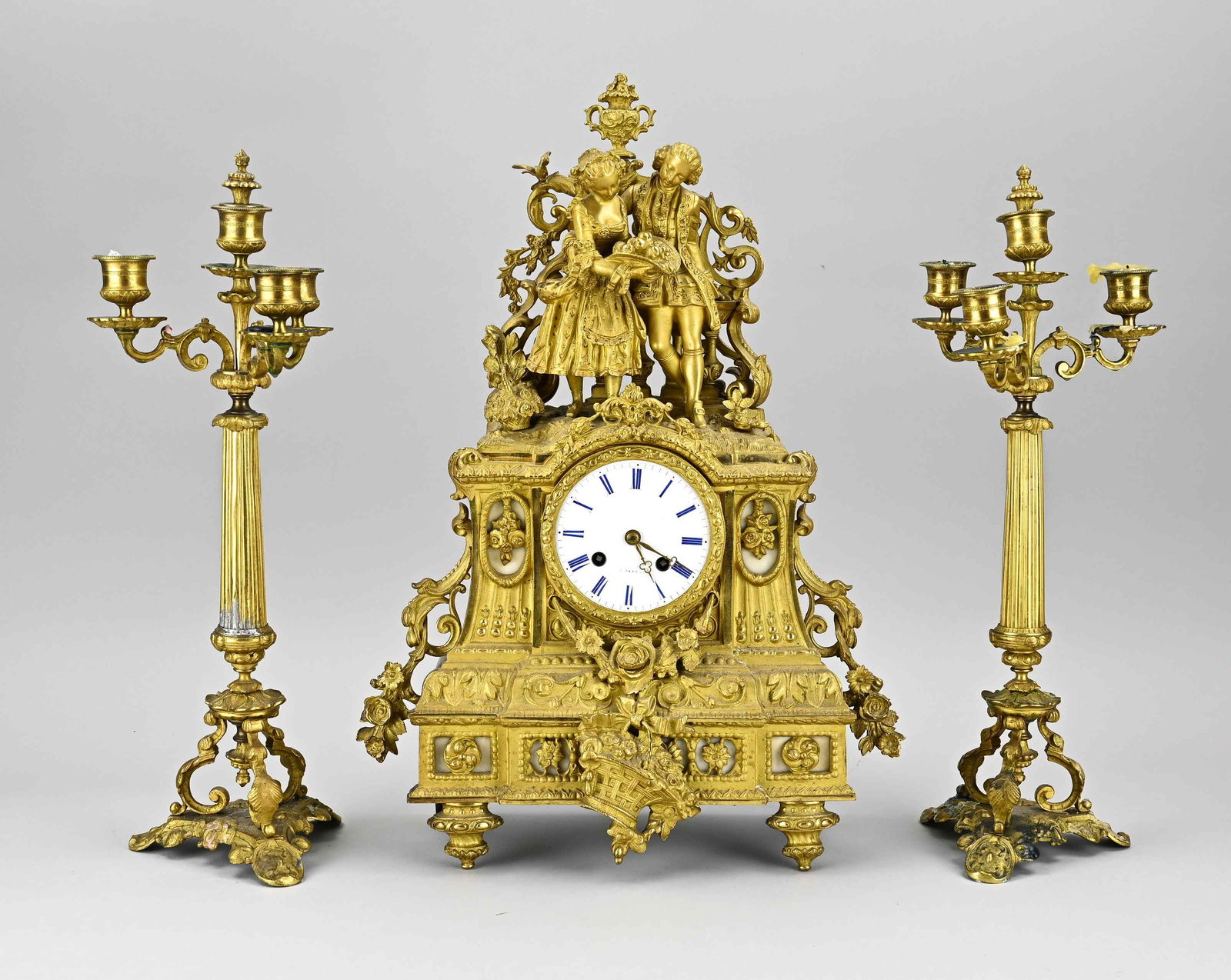 3-piece French clock set, 1850: Three-piece 19th century French gilt bronze clock set with candlesticks. Romantic couple with fruit. Eight-day movement, half-hourly striking, spring pendulum. Pendulum lacks lens. One candlestick