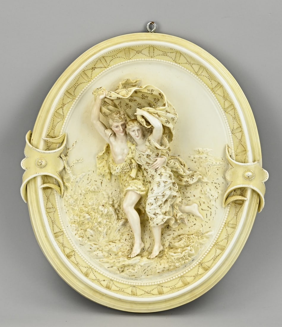 Porcelain wall plaque, 1880: Antique porcelain wall plaque with two figures in the wind. Circa 1880. Damaged. Dimensions: H 41 x W 36 cm. In reasonable condition.