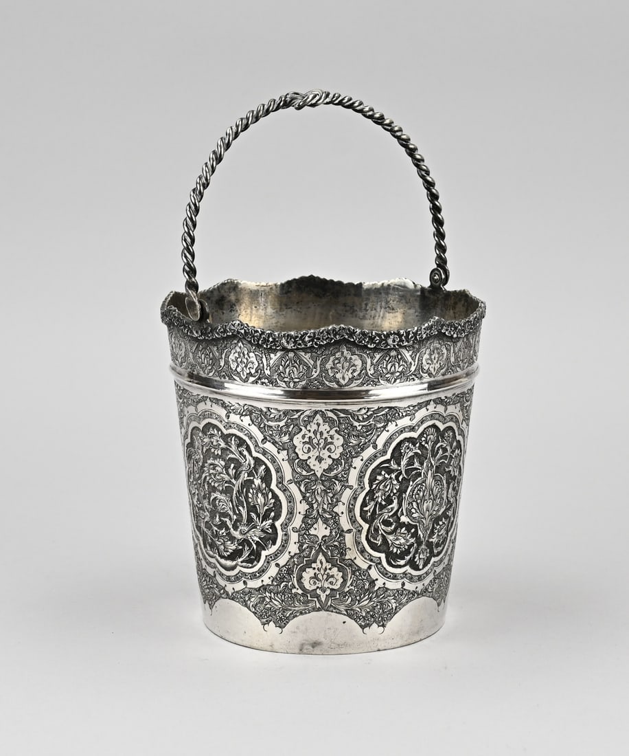 Silver Ice Bucket Isfahan: Silver ice bucket with a decorated edge with a soldered flower edge. The bucket is further decorated with Persian work. The bucket has a twisted handle with knot. approx. 573 grams. ø14x25 cm. In goo
