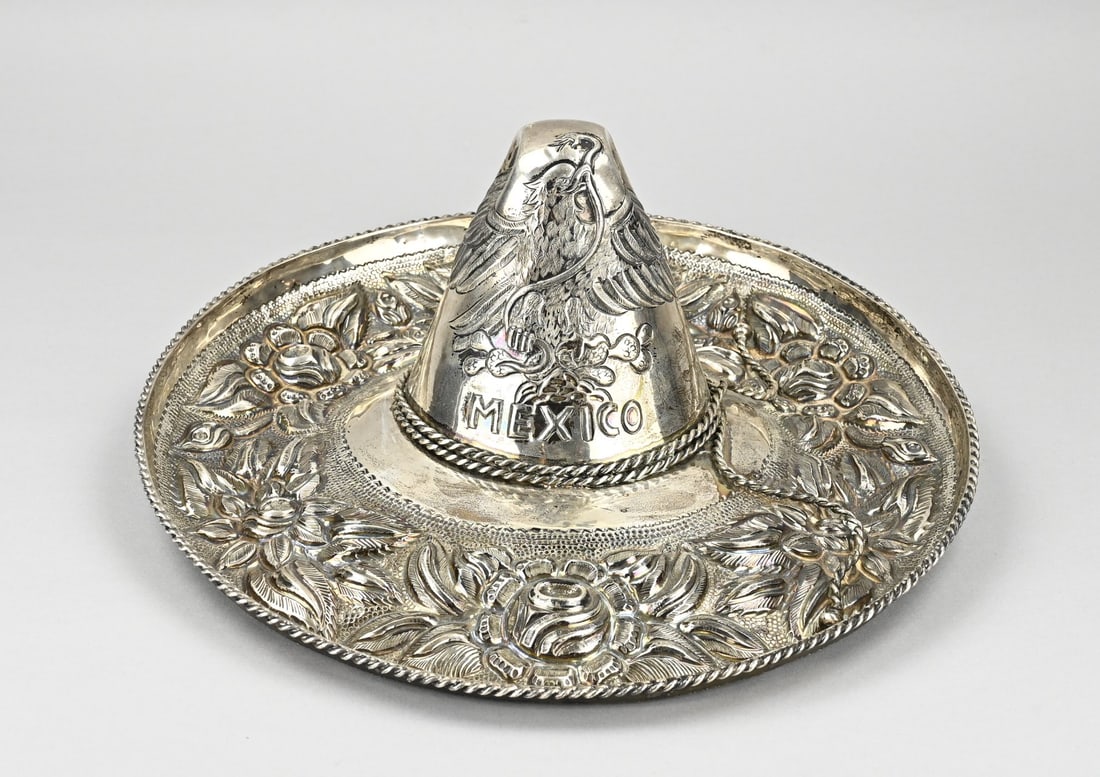 Large silver sombrero: Large silver Mexican sombrero, 925/000, with a richly decorated edge and decorated with an eagle and MEXICO. The sombrero has a twisted edge. approx. 1600 grams. ø 40x17cm. In good condition.