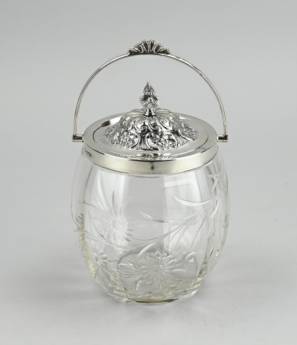 Cookie jar with silverware: Crystal cookie jar with a silver collar, lid and handle, 925/000. Crystal jar decorated with floral grinding, provided with a silver rim and handle with fan work. The cookie jar has a round silver